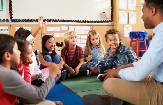 Stock photo elementary school kids and teacher sit cross legged on floor.